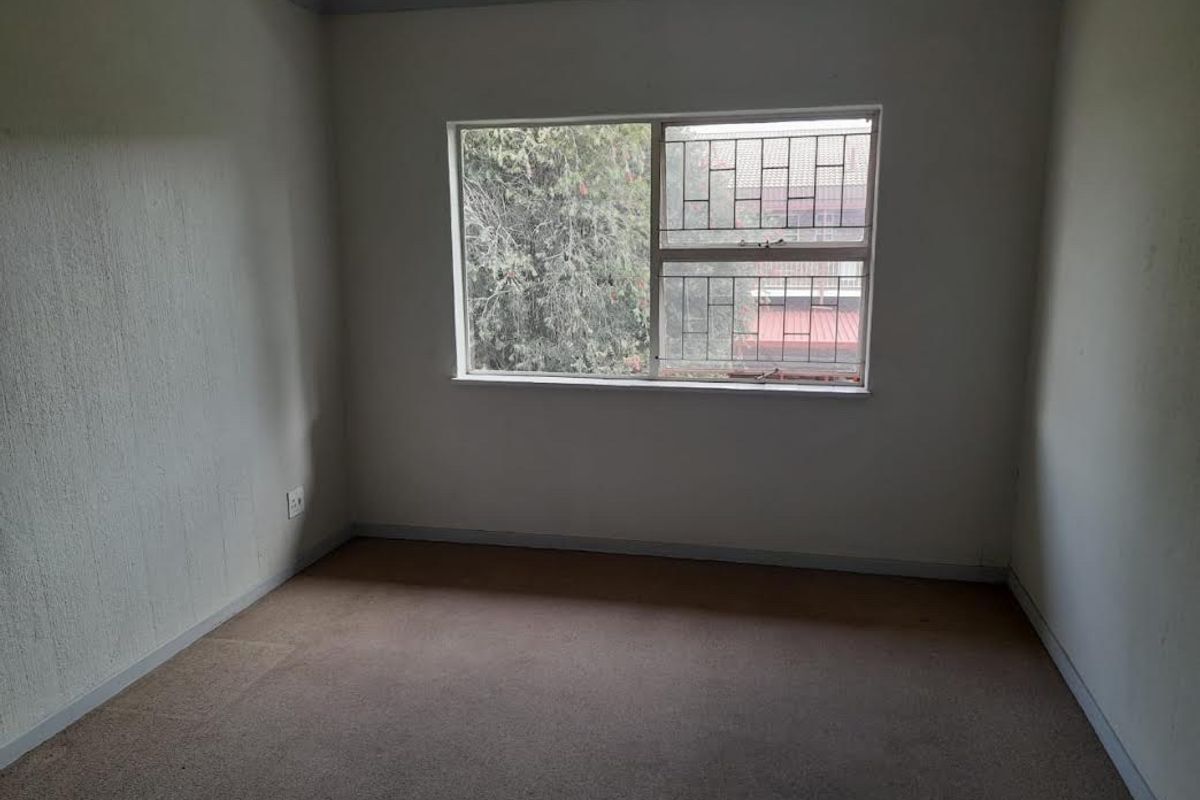 An empty bedroom featuring carpeted flooring and a window fitted with security bars, offering a blank canvas for personalization.