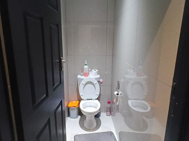 A compact, modern bathroom featuring full-height wall tiling, a standard toilet, and a bidet spray fixture.