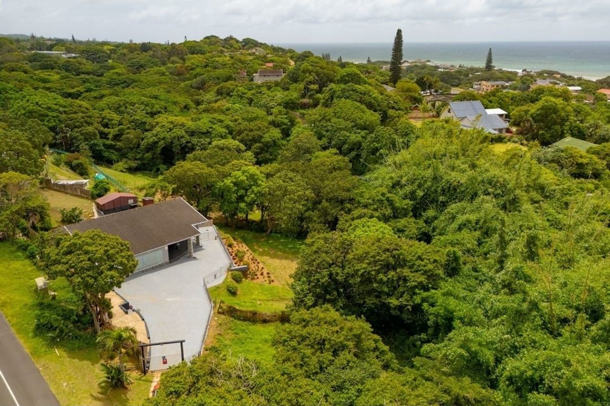 Aerial view of the property showcasing the house, paved driveway, and surrounding lush greenery with a distant ocean view.