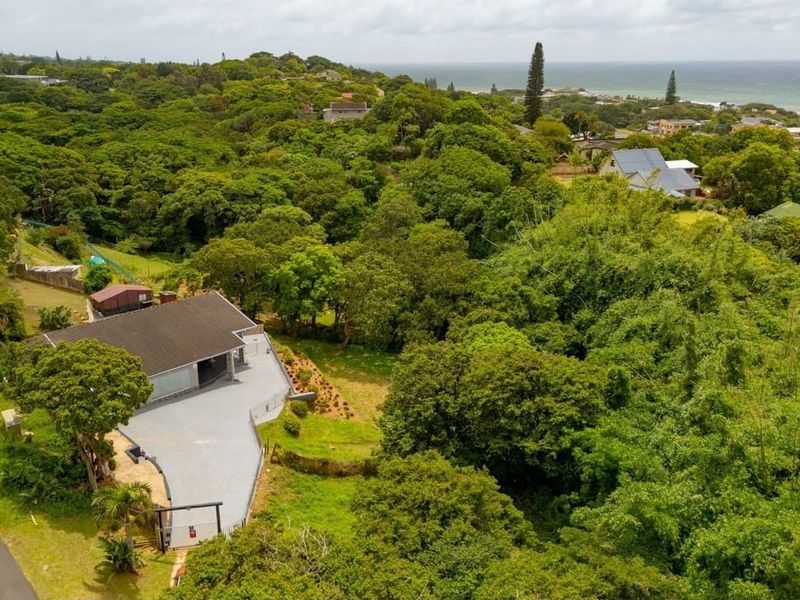 Aerial view of the property showcasing the house, paved driveway, and surrounding lush greenery with a distant ocean view.
