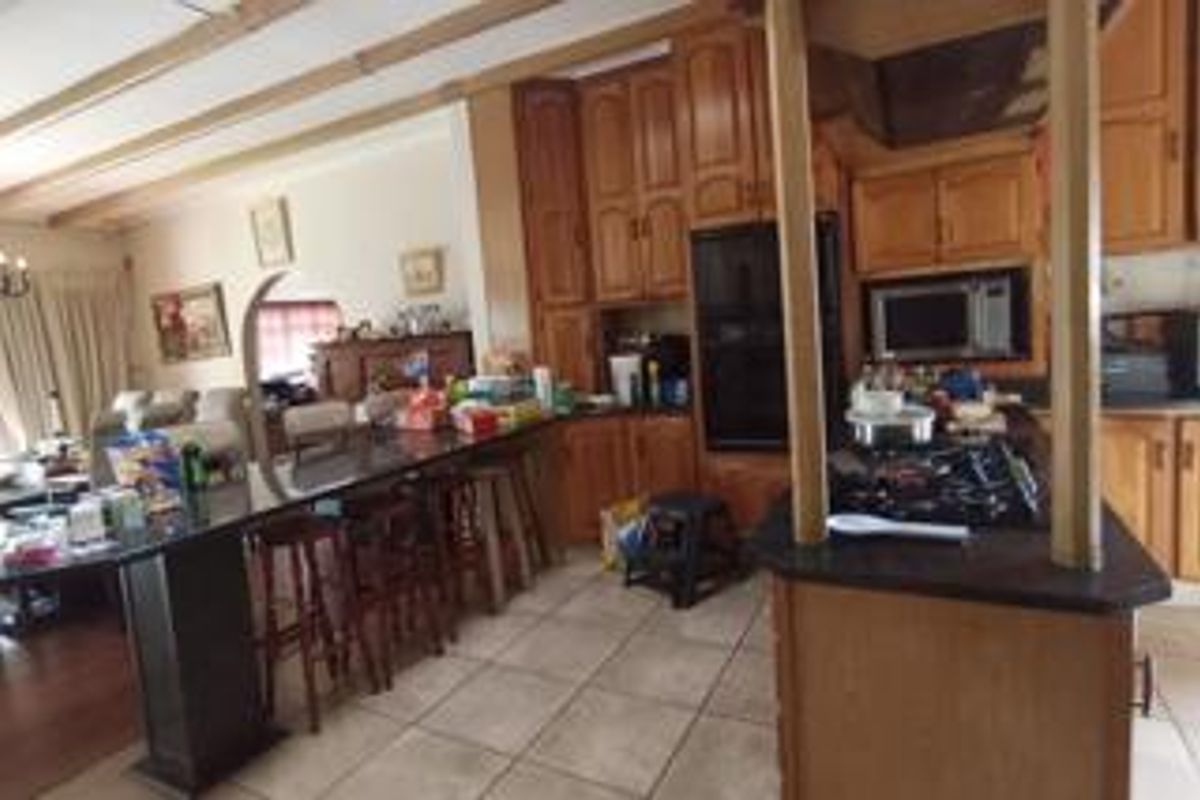 Open plan kitchen and living area featuring wooden cabinetry, granite countertops, built-in appliances, and exposed ceiling beams.