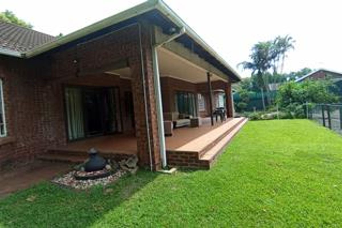 A spacious covered brick patio area overlooking a well-maintained garden, featuring tiled flooring and direct access to the home via sliding glass doors.