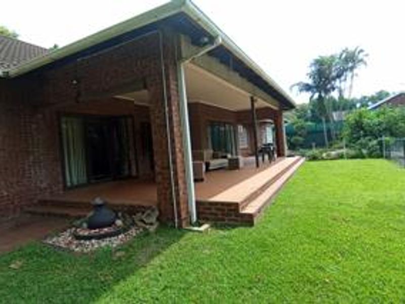 A spacious covered brick patio area overlooking a well-maintained garden, featuring tiled flooring and direct access to the home via sliding glass doors.
