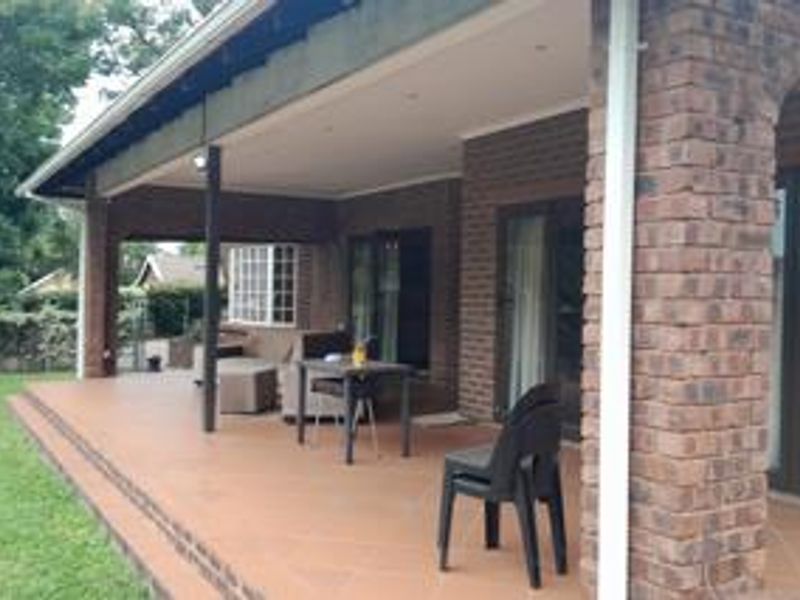 A spacious covered patio featuring tiled flooring, brick pillars, and recessed lighting, providing a seamless transition to the garden area.