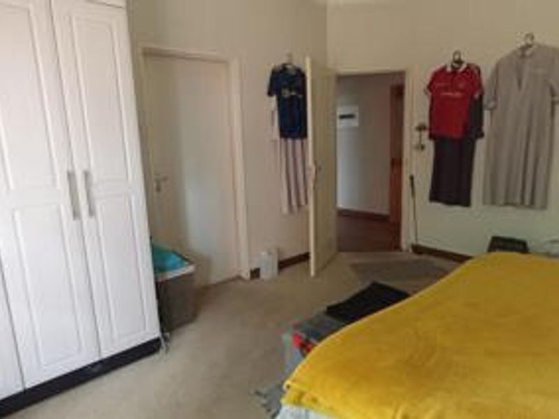 A bedroom featuring a white built-in wardrobe and neutral wall finishes, providing a functional space with direct access to an adjoining hallway.