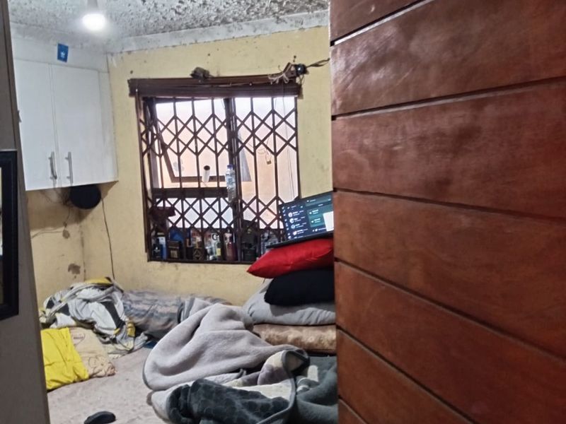 A bedroom featuring a textured ceiling, built-in cabinetry, and a security gate on the window, requiring cosmetic updates and repairs to walls and ceiling.