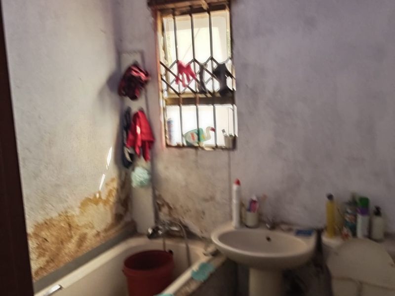 A dated bathroom featuring a bathtub, pedestal basin, and toilet, requiring significant renovation and repair to the wall finishes.