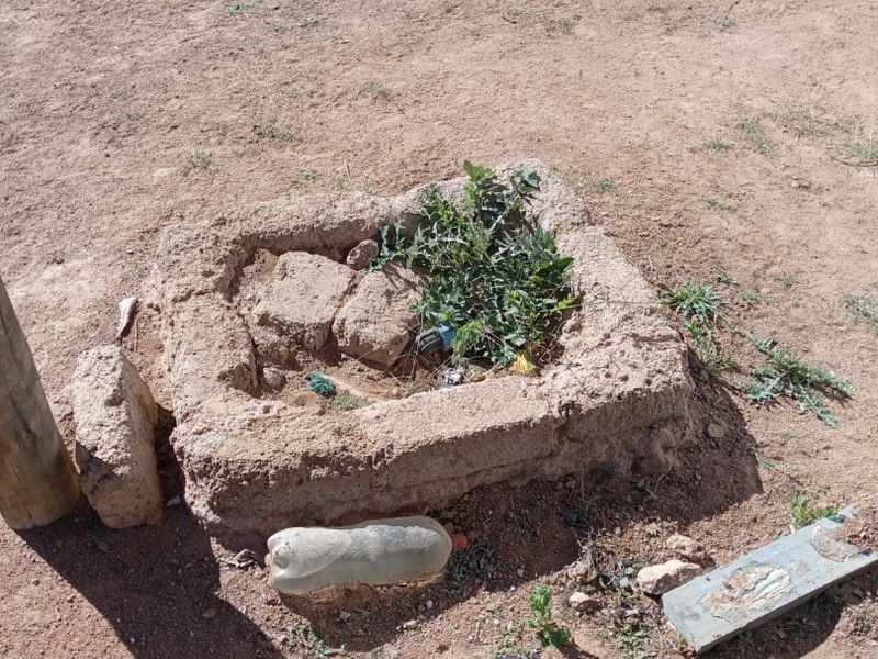 An outdoor area featuring a small, weathered stone masonry border structure set within an unmaintained dirt ground surface.