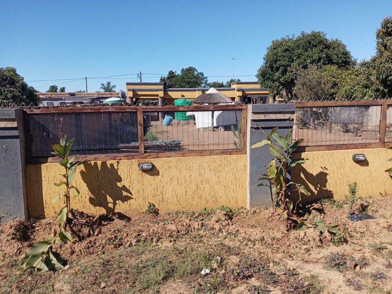 A view of the rear boundary wall featuring textured plaster, integrated exterior lighting, and wire mesh fencing enclosing the property perimeter.