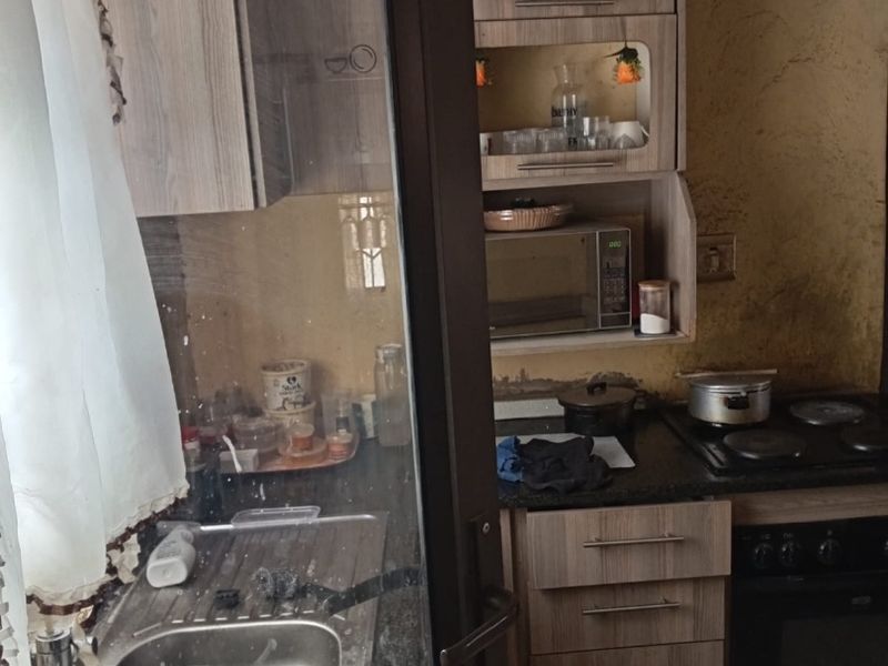 A compact kitchen featuring built-in cabinetry, granite countertops, and integrated appliances, currently requiring significant wall repairs and cosmetic updates to improve functionality and aesthetic appeal.