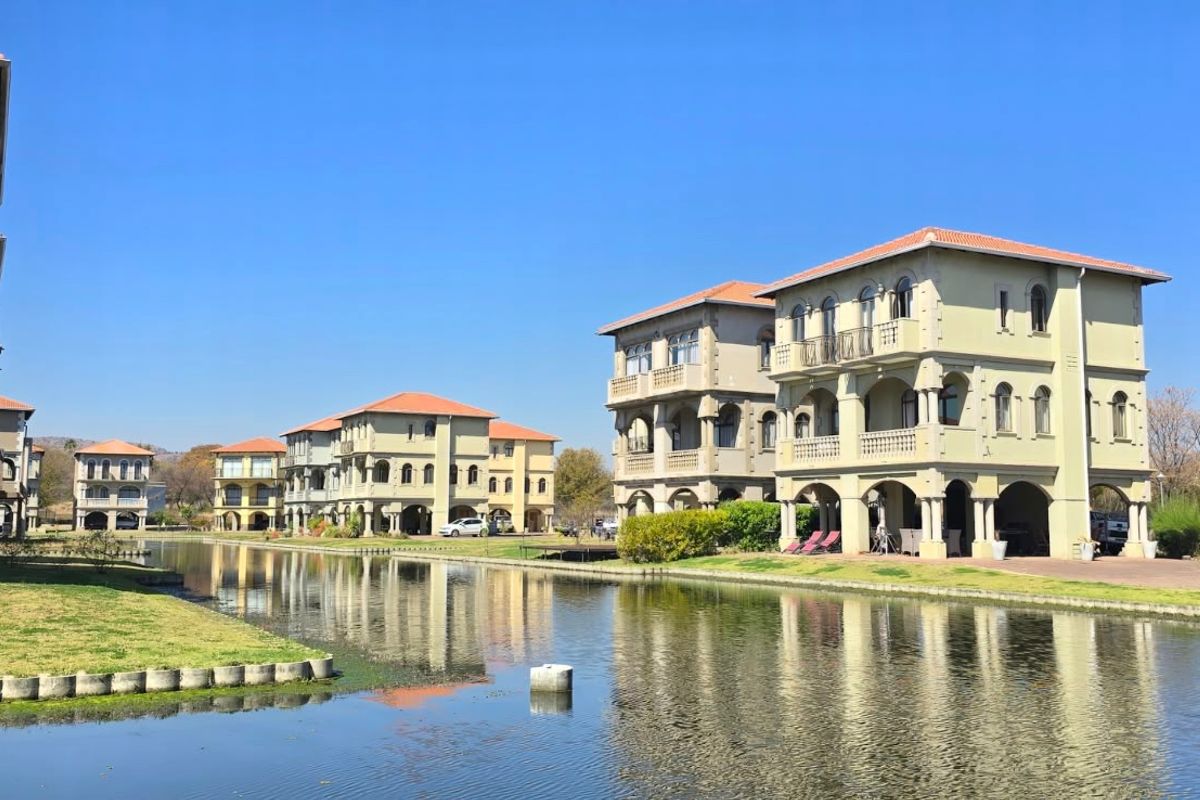 A scenic view of multi-story residential villas featuring Mediterranean-style architecture, arched balconies, and terracotta roofs, situated along a tranquil canal.