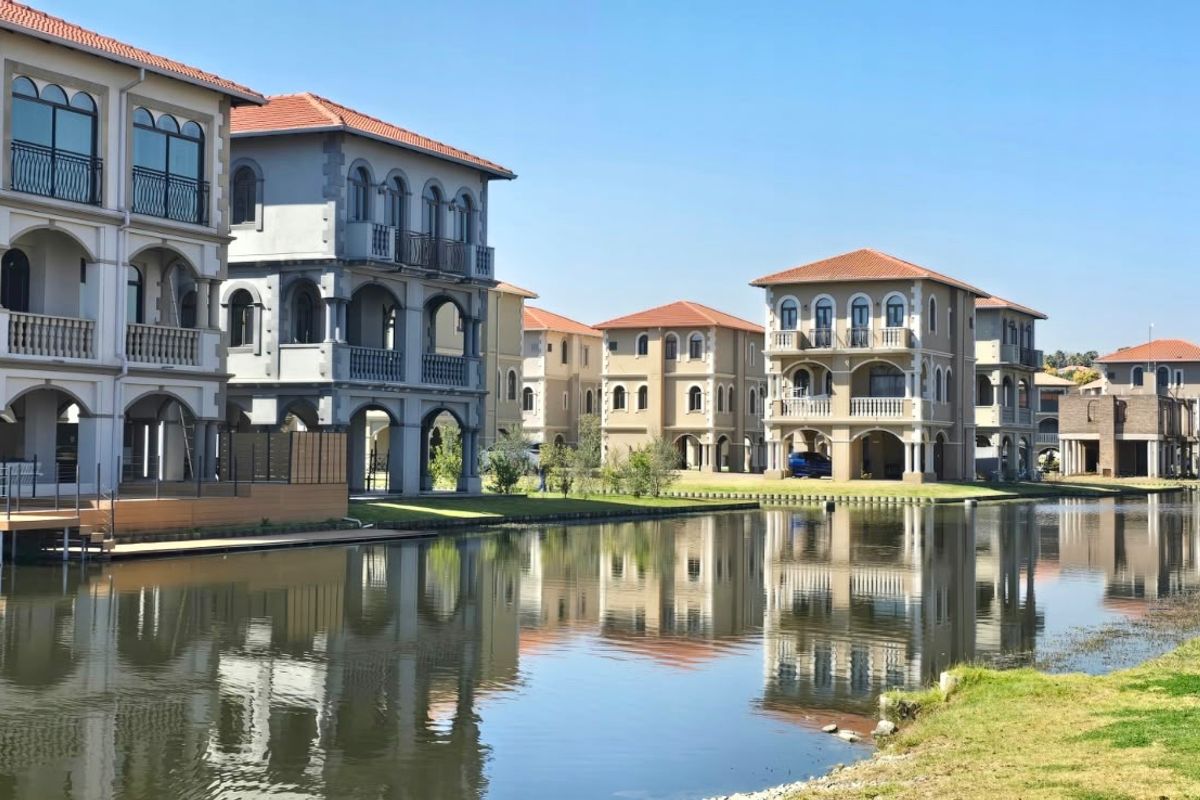 A scenic view of multi-story residential properties featuring Mediterranean-style architecture with balconies and arched detailing, situated directly along a tranquil canal.