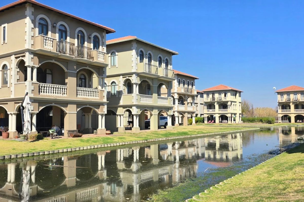 A row of multi-story residential units featuring classic architectural details, balconies, and arched windows, overlooking a tranquil canal and landscaped grounds.