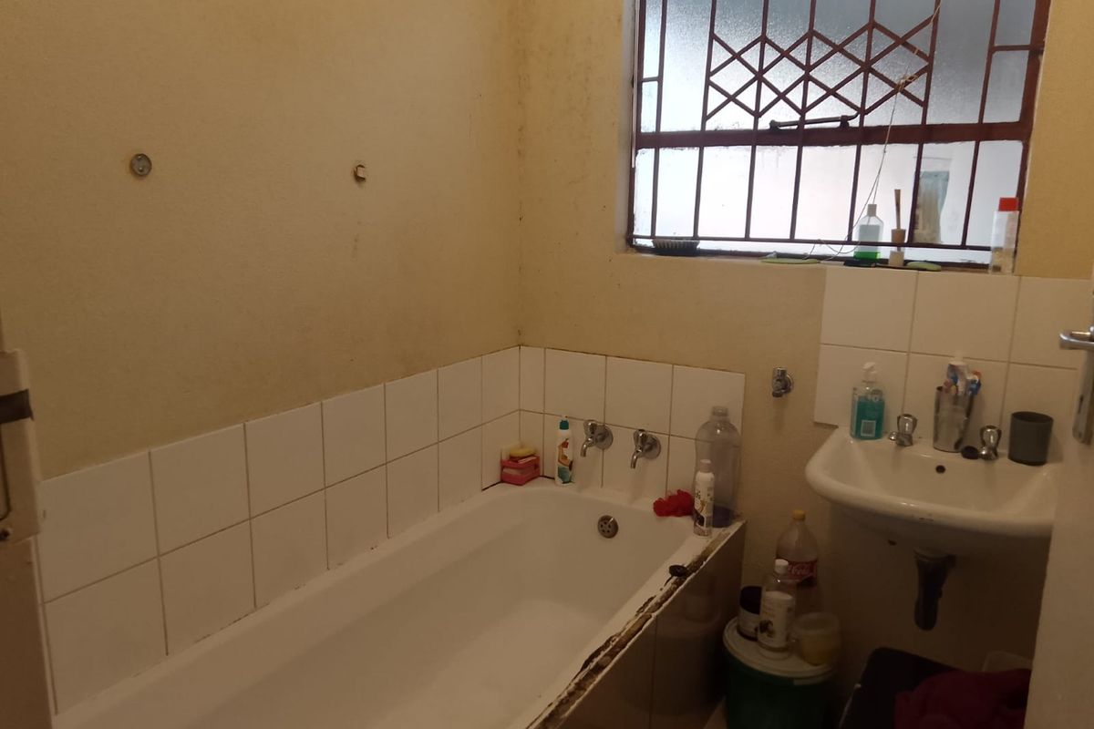 A dated bathroom featuring a standard bathtub and wall-mounted basin, requiring cosmetic updates and repairs to finishes.