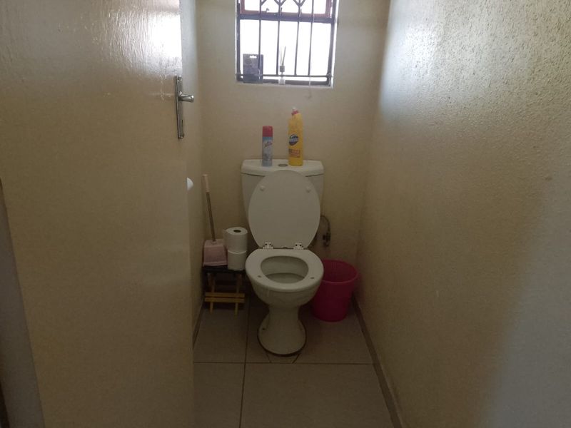A compact bathroom featuring a standard toilet, tiled flooring, and a window with security bars.