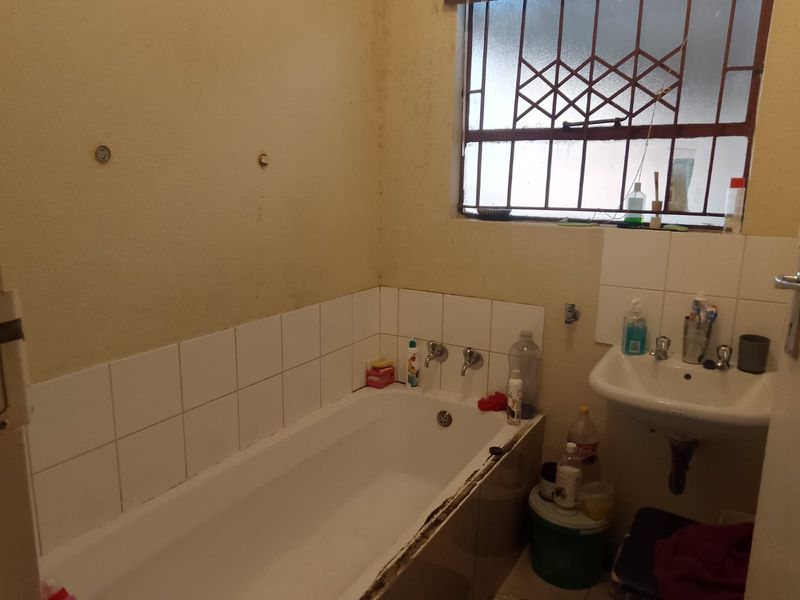 A dated bathroom featuring a standard bathtub and wall-mounted basin, requiring cosmetic updates and repairs to finishes.