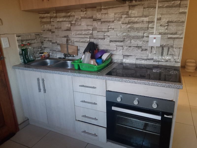 Compact kitchen featuring built-in cabinetry, a double bowl sink, electric hob, and oven with a decorative stone-look tile splashback.