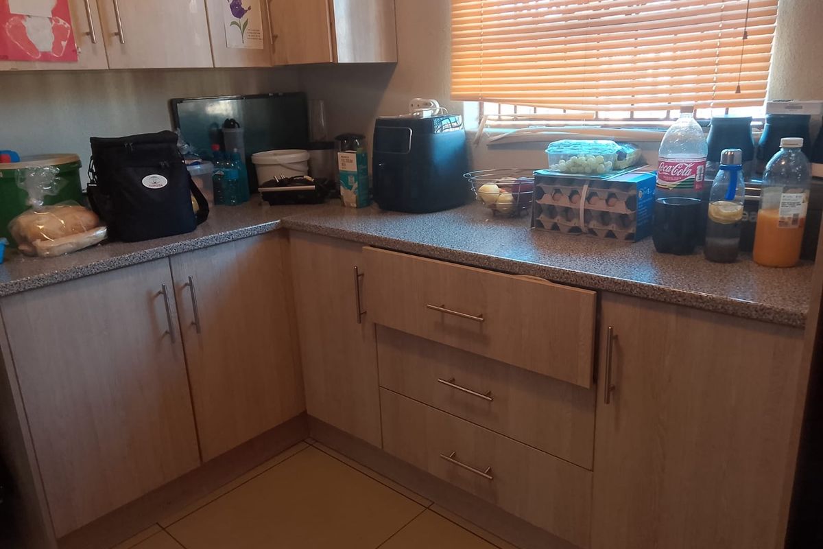 A functional kitchen area featuring light wood-tone cabinetry, laminate countertops, and tiled flooring, currently showing signs of daily use.