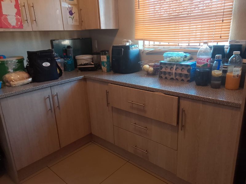 A functional kitchen area featuring light wood-tone cabinetry, laminate countertops, and tiled flooring, currently showing signs of daily use.