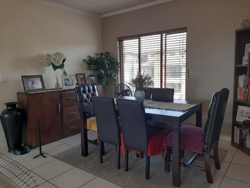 A functional dining area featuring neutral wall tones, tiled flooring, and large windows fitted with venetian blinds for natural light control.