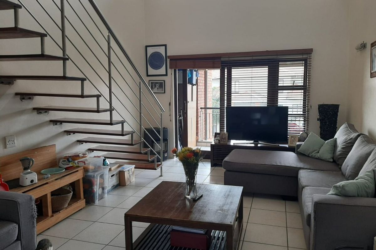 Open-plan living area featuring a modern staircase with metal balustrades, tiled flooring, and access to a balcony through a sliding door.