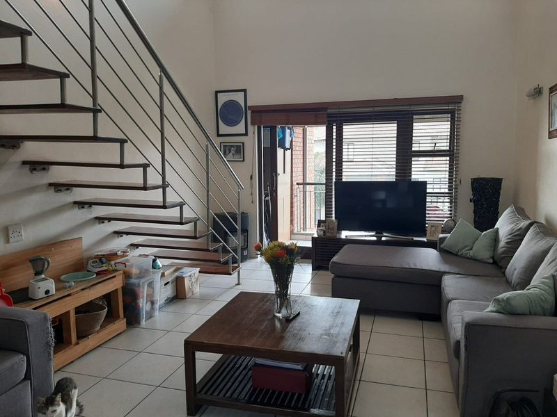 Open-plan living area featuring a modern staircase with metal balustrades, tiled flooring, and access to a balcony through a sliding door.