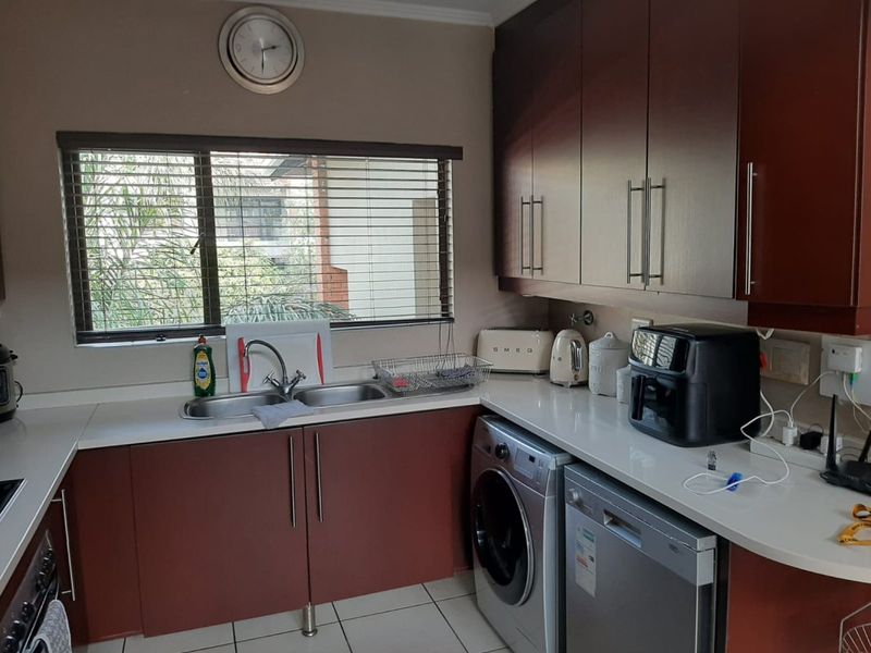 A functional kitchen featuring dark wood cabinetry, white countertops, a double bowl sink, and tiled flooring with a window overlooking the exterior.