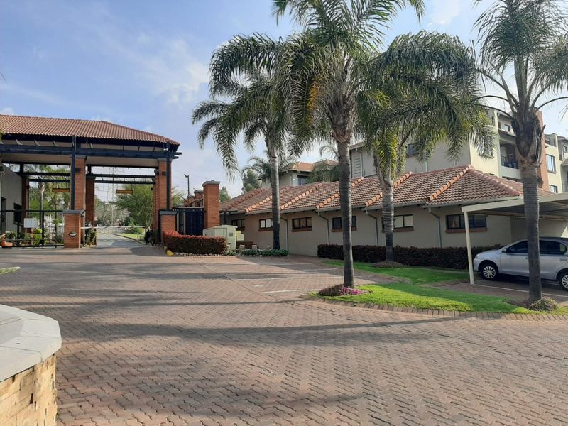 View of the apartment complex entrance featuring a paved driveway, security gate, and covered parking area with established landscaping.