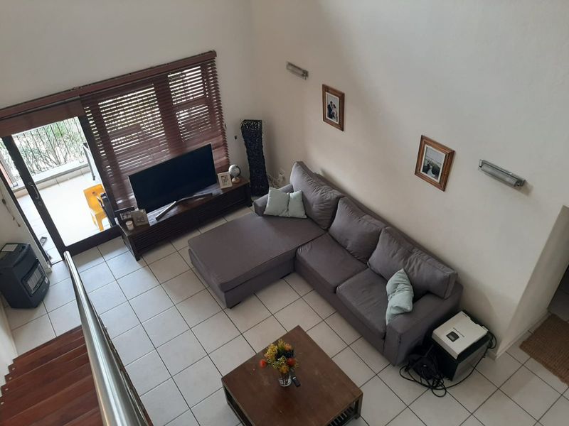 Spacious double-volume living area featuring tiled flooring, large sliding doors with wooden blinds, and direct access to an outdoor balcony.