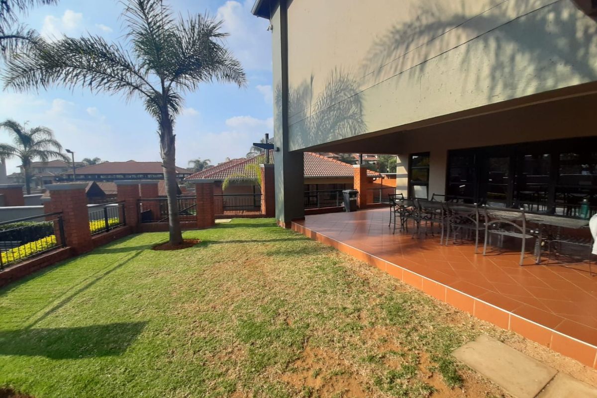 A spacious rear patio with tiled flooring, overlooking a private lawn area enclosed by brick boundary walls and metal railings.
