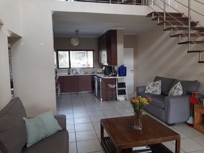 Open plan living area featuring a kitchen with built-in cabinetry, tiled flooring, and a staircase leading to a mezzanine level.