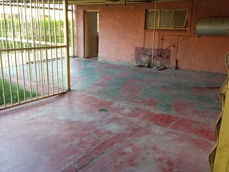 A covered outdoor patio area featuring a painted concrete floor, metal security screening, and exposed structural elements in need of maintenance and refurbishment.