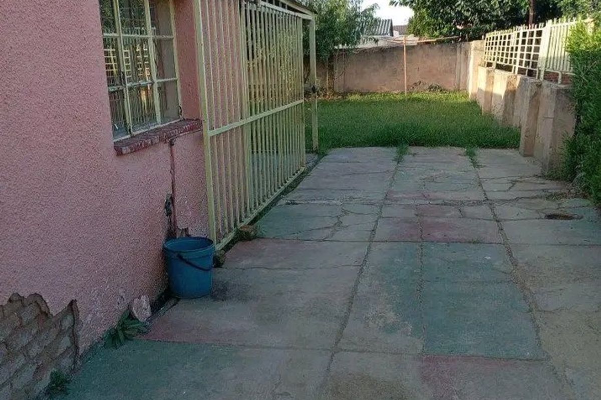 Rear exterior view showing a paved patio area, security gate, and a small garden with boundary walling.
