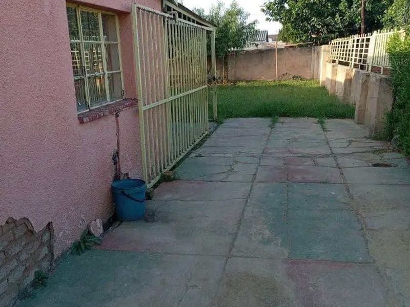 Rear exterior view showing a paved patio area, security gate, and a small garden with boundary walling.