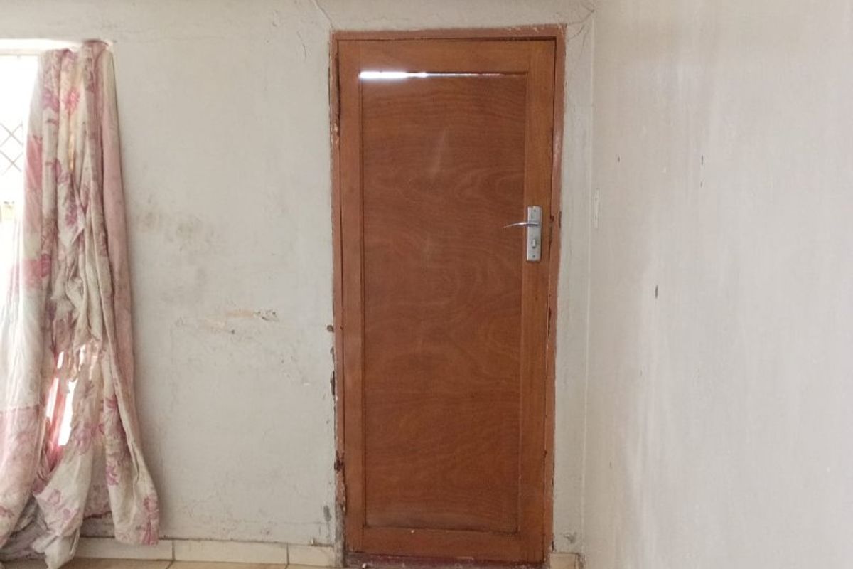 An interior living space featuring tiled flooring and a wooden door, currently in need of wall repairs and cosmetic refurbishment.