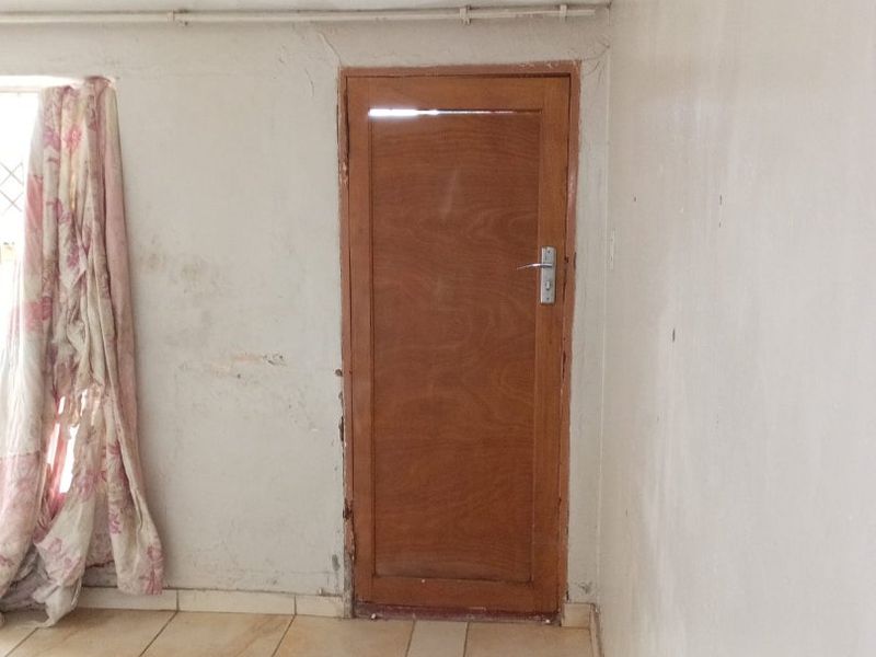 An interior living space featuring tiled flooring and a wooden door, currently in need of wall repairs and cosmetic refurbishment.
