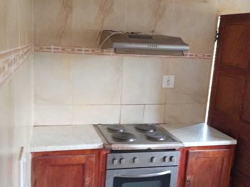 A compact kitchen area featuring built-in wooden cabinetry, an electric oven and hob, and a tiled splashback with an extractor fan.