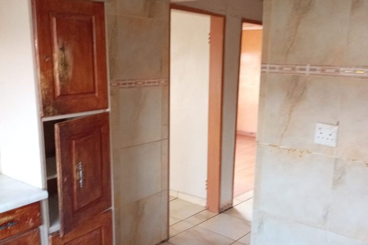 A kitchen area featuring tiled walls and flooring with built-in wooden cabinetry showing signs of wear.