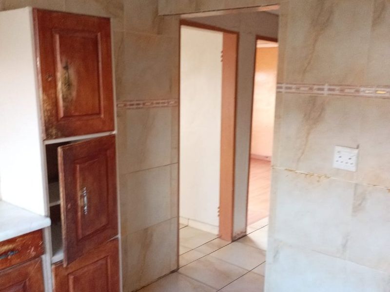 A kitchen area featuring tiled walls and flooring with built-in wooden cabinetry showing signs of wear.