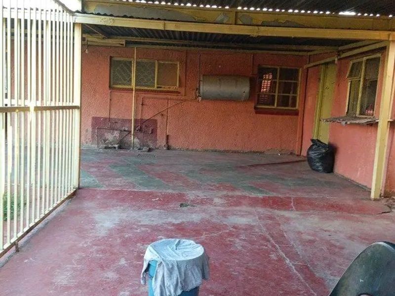 A covered outdoor patio area featuring a corrugated iron roof, painted concrete flooring, and an external wall-mounted electric geyser.