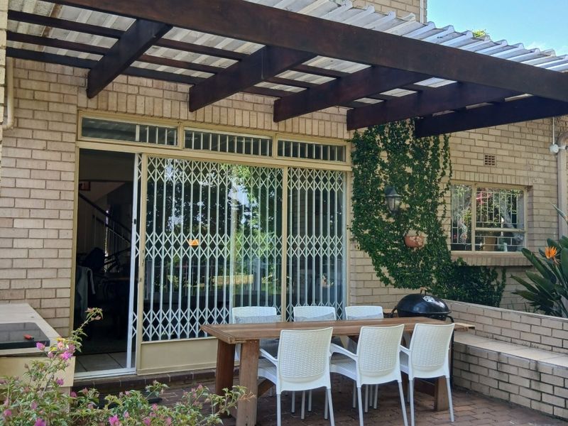 Rear exterior view featuring a paved patio area with a timber pergola, brick facade, and secure sliding door access to the home.