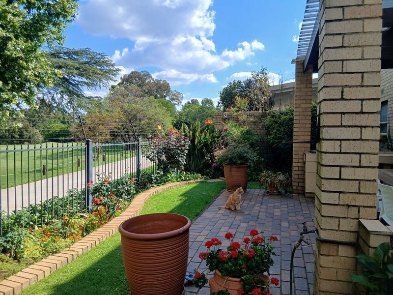 A paved patio area featuring a brick pillar, pergola structure, and established garden beds overlooking a green space.