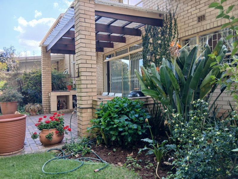 Covered patio area featuring a built-in braai, brick pillars, and a timber pergola, providing a functional outdoor entertainment space adjacent to the garden.
