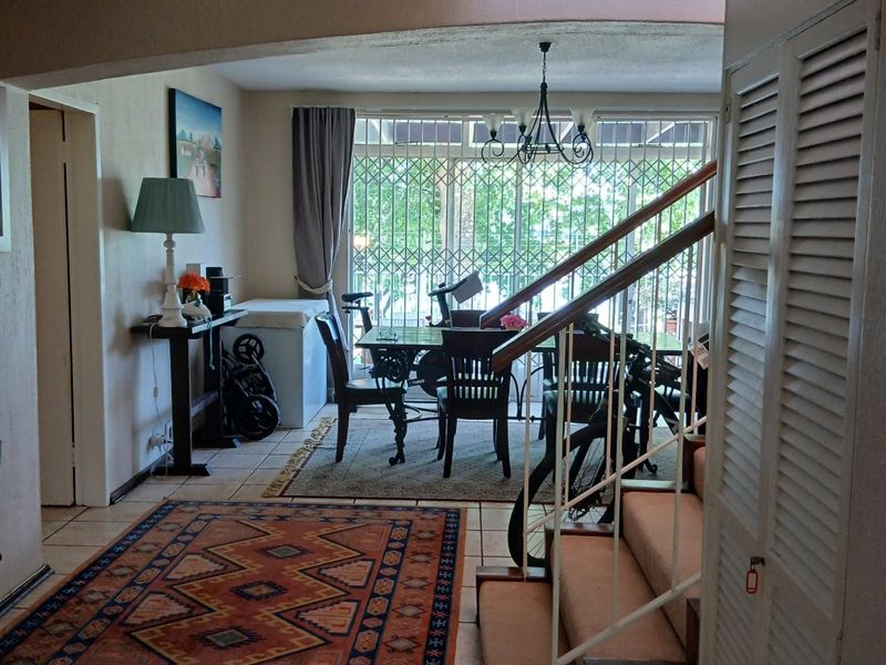 Open plan living and dining area featuring tiled floors, a central staircase with carpeted steps, and large windows with security gates.