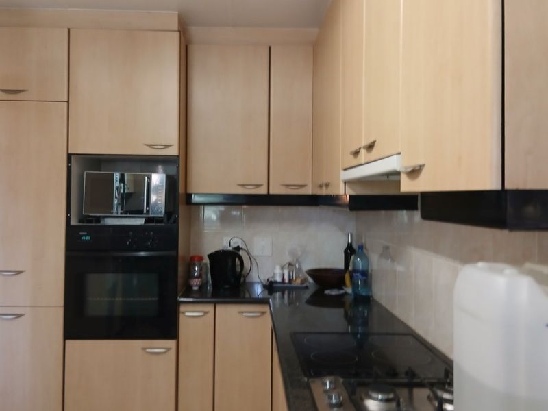 A functional kitchen featuring light wood-tone cabinetry, granite countertops, a built-in oven, microwave, and a gas cooktop with an integrated extractor fan.