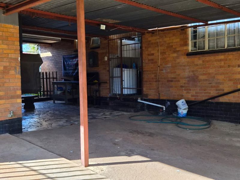 A functional, open-sided garage area featuring brick walls, a corrugated metal roof, and concrete flooring, providing covered parking or utility space.