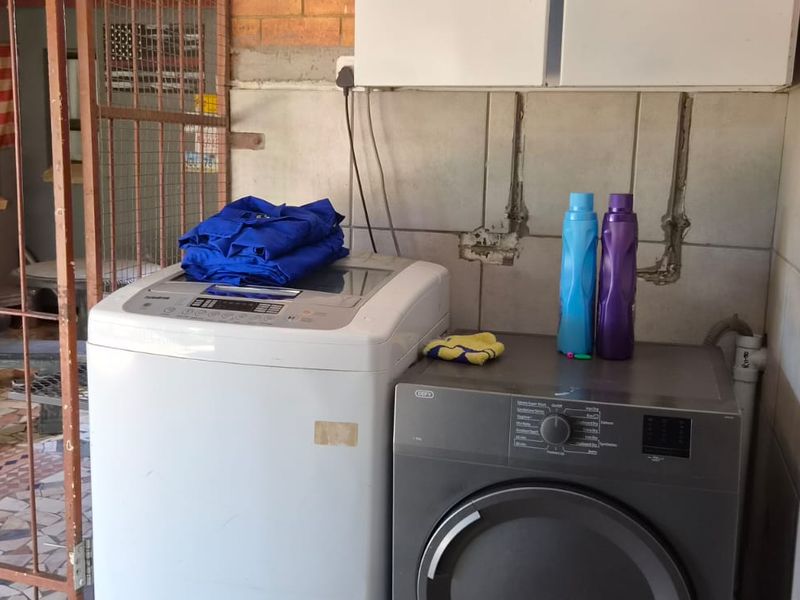 A functional laundry area featuring tiled walls, exposed brickwork, and dedicated plumbing and electrical connections for laundry appliances.