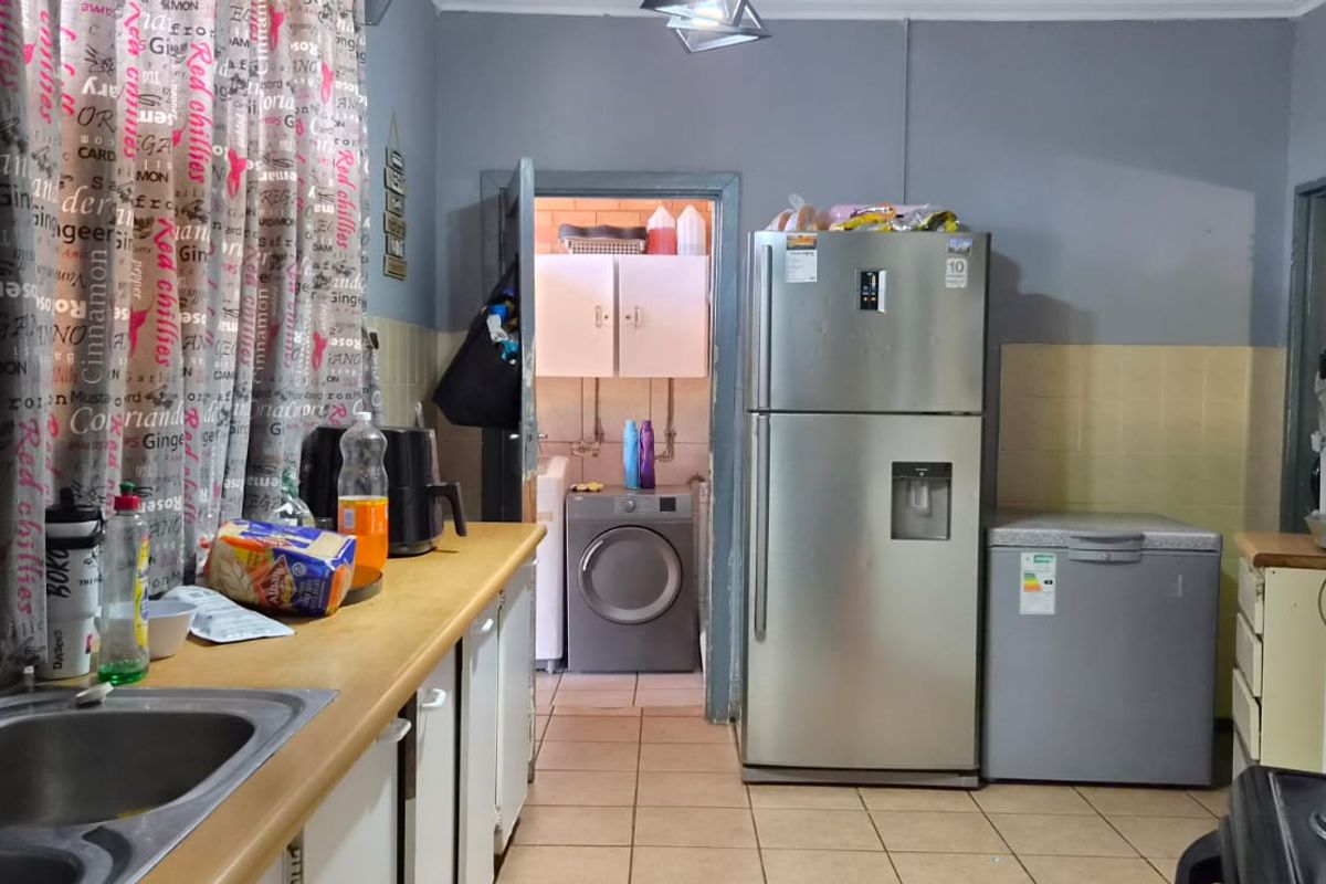 A functional kitchen featuring tiled splashbacks, built-in cabinetry, and a stainless steel sink, with an adjacent laundry area visible through the doorway.