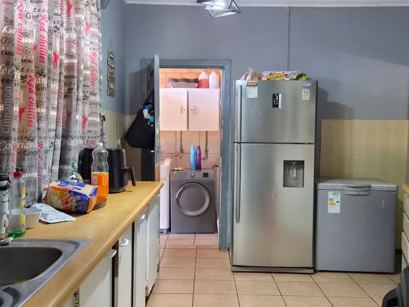 A functional kitchen featuring tiled splashbacks, built-in cabinetry, and a stainless steel sink, with an adjacent laundry area visible through the doorway.