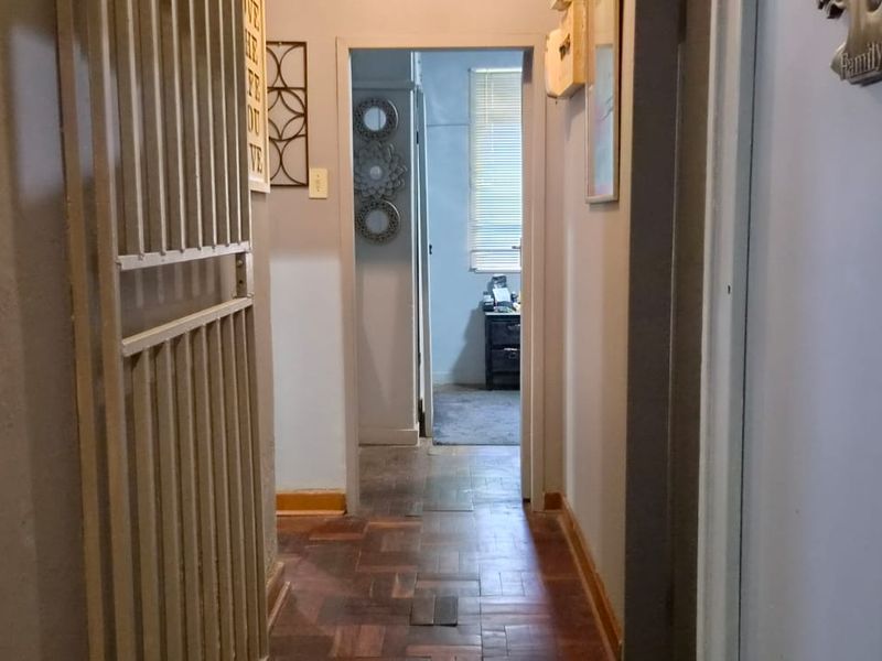 A narrow interior hallway featuring traditional parquet flooring and a metal security gate, connecting multiple rooms within the home.